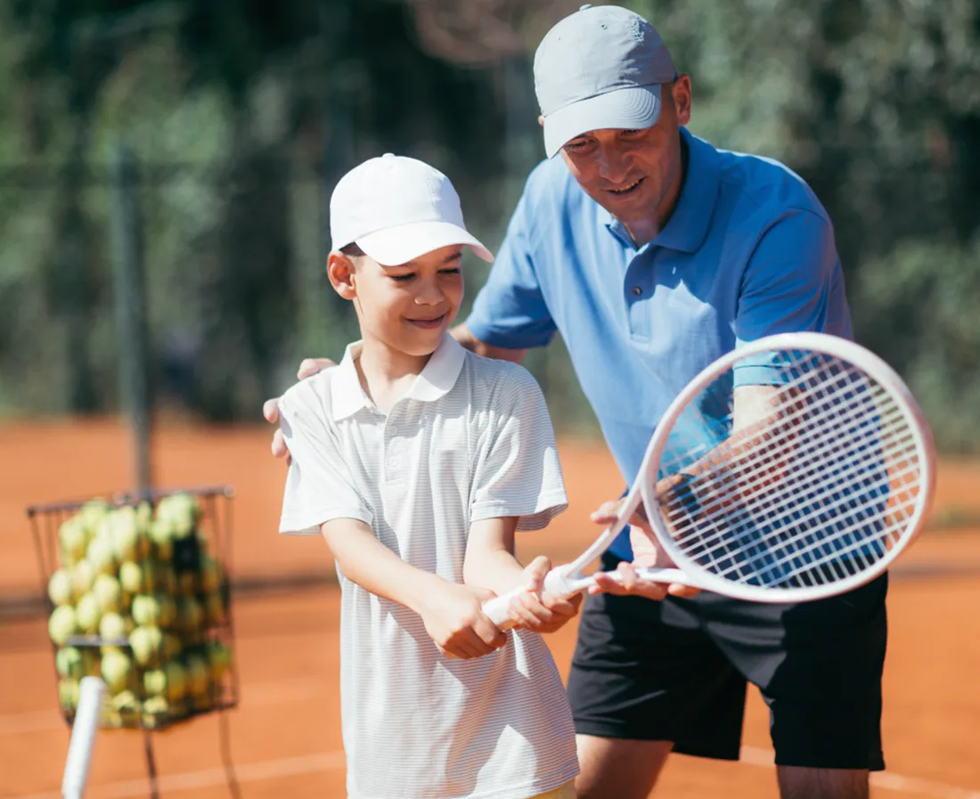 A tennis coach guiding a young player through a swing